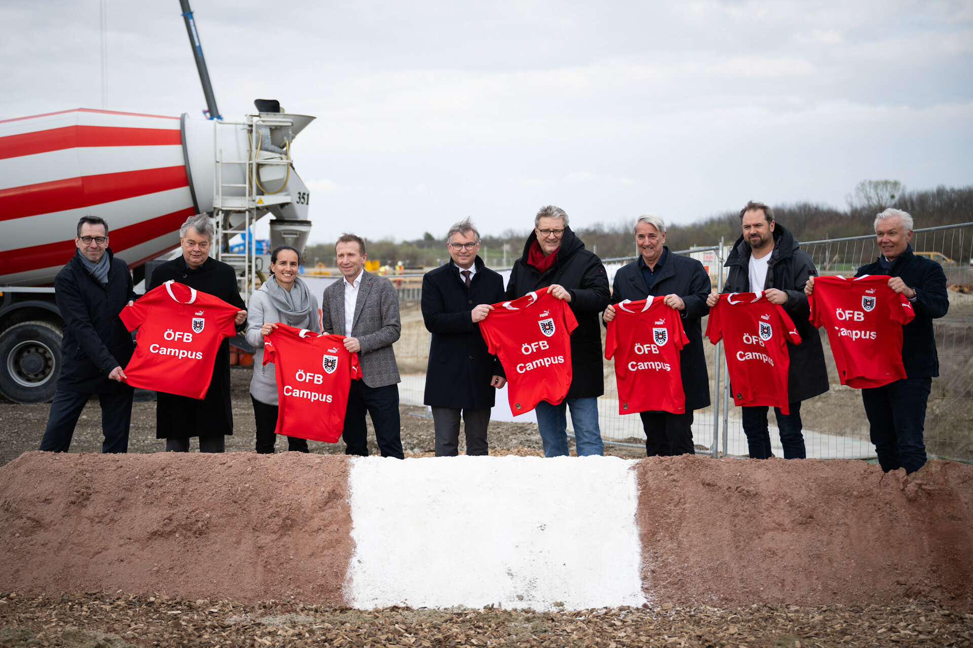Mehrere Personen mit roten Trikots, im Hintergrund ein Betonmischwagen