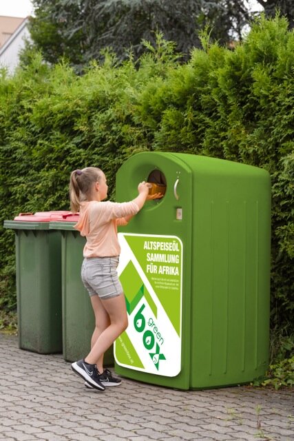 ein Mädchen wirft draußen einen Behälter in eine Box