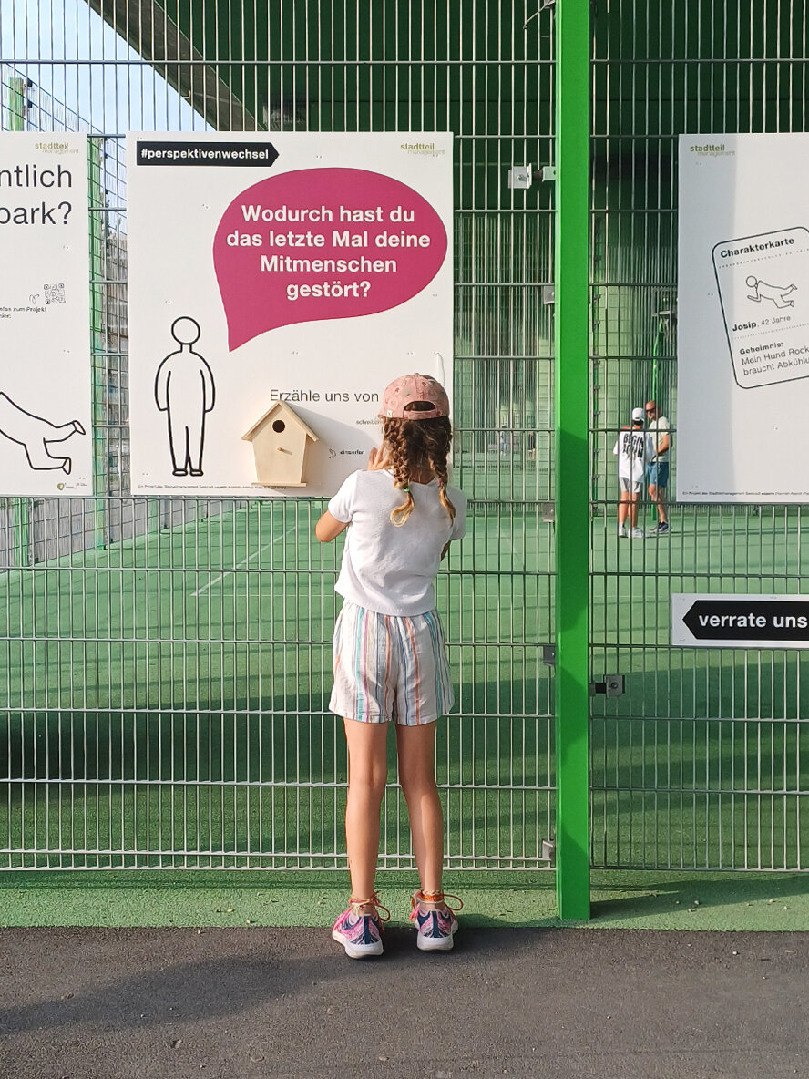 Ein grüner Zaun mit Plakaten darauf.