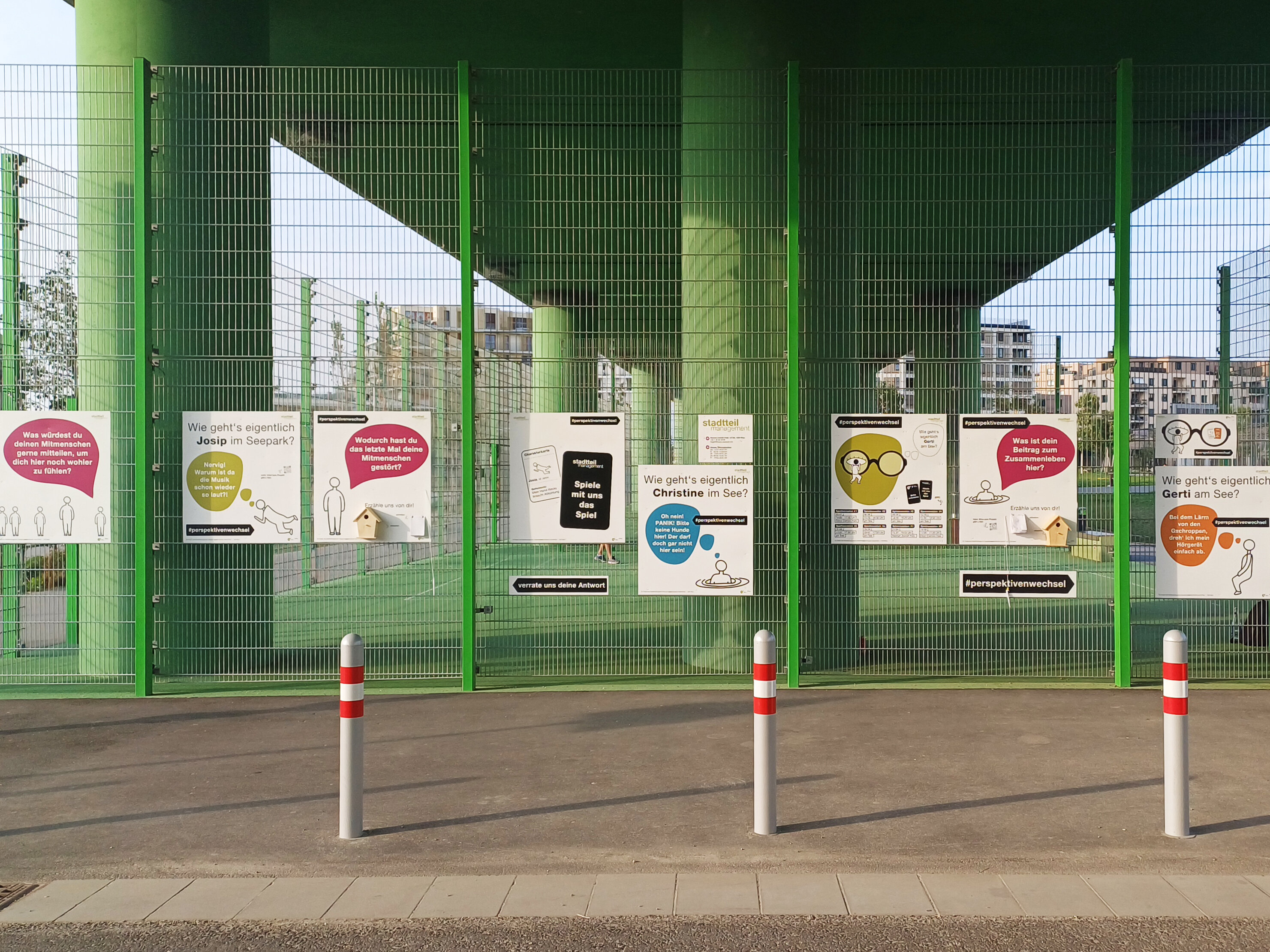 Ein grüner Zaun mit Plakaten darauf.