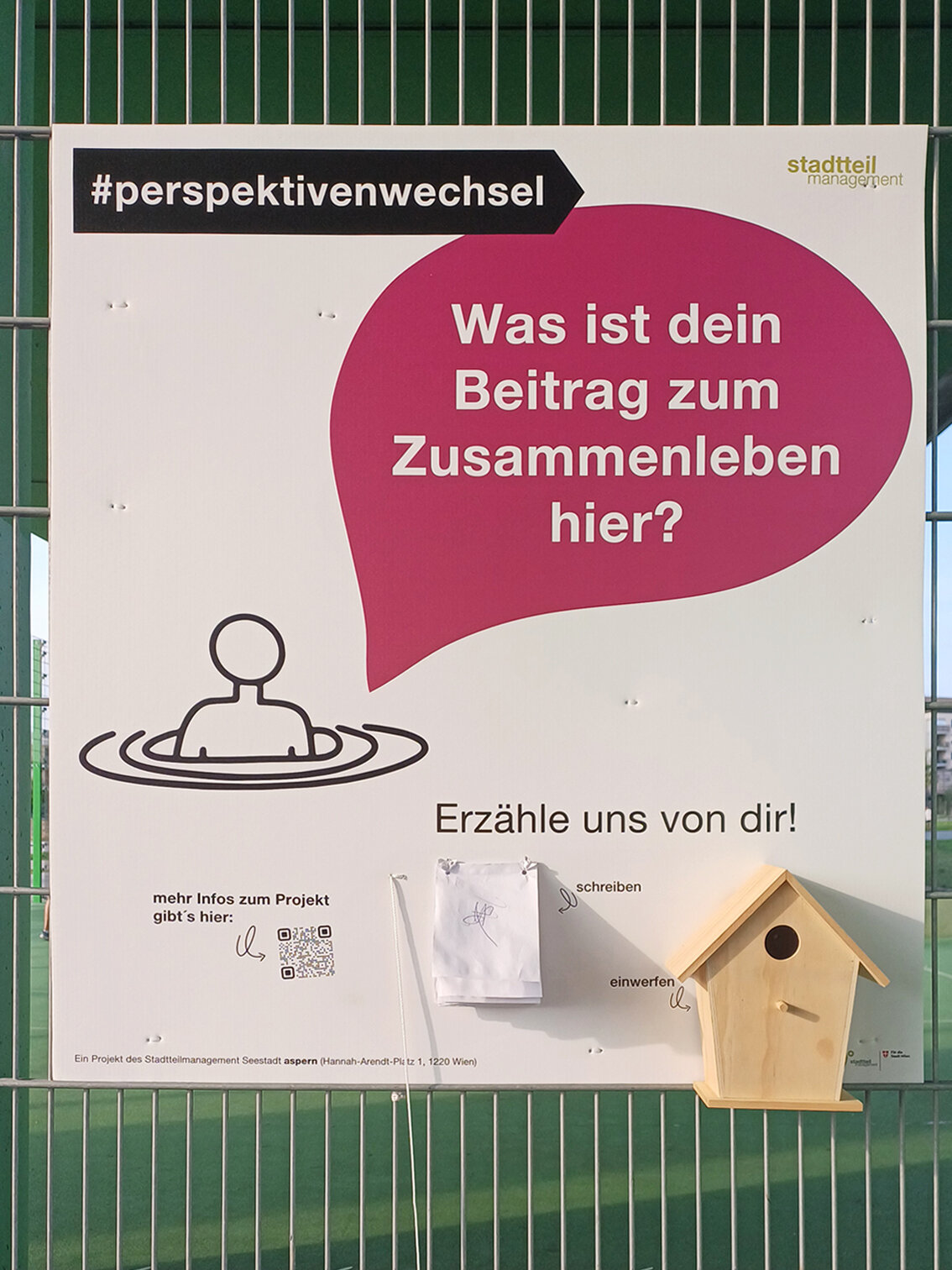 Ein grüner Zaun mit Plakaten darauf.