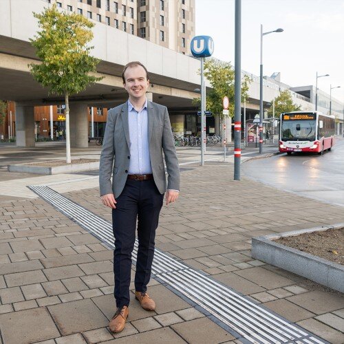 Ivan Hlavina stehen auf einem Platz mit Pflastersteinen. Hinter ihn ein U-Bahn Schild.