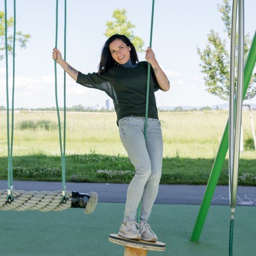 Lenka Recek stehend auf einer Schaukel. Hier ihr grüne Wiese.