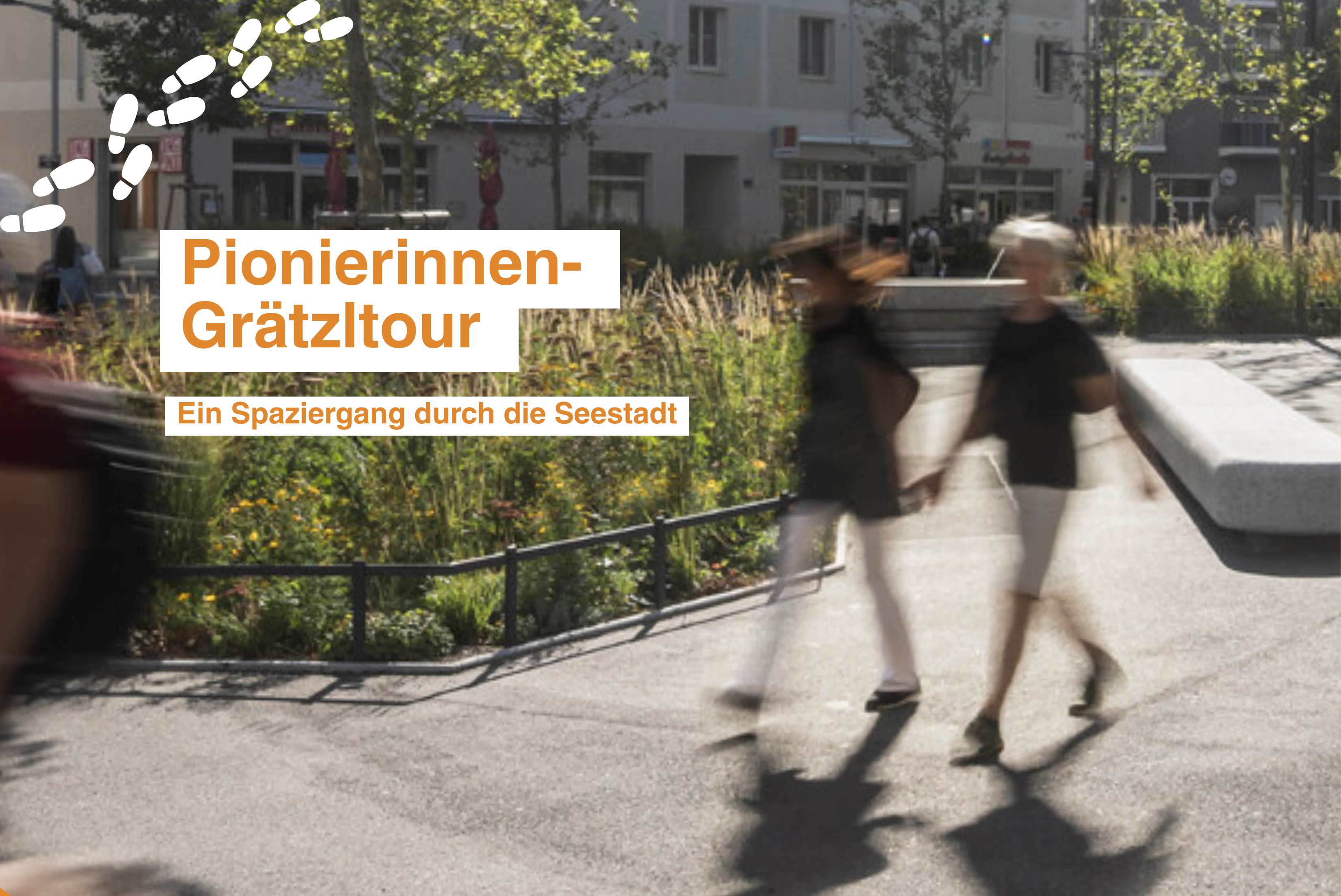 Platz in der Seestadt mit Bäumen und Passanten, die durch das Bild gehen.