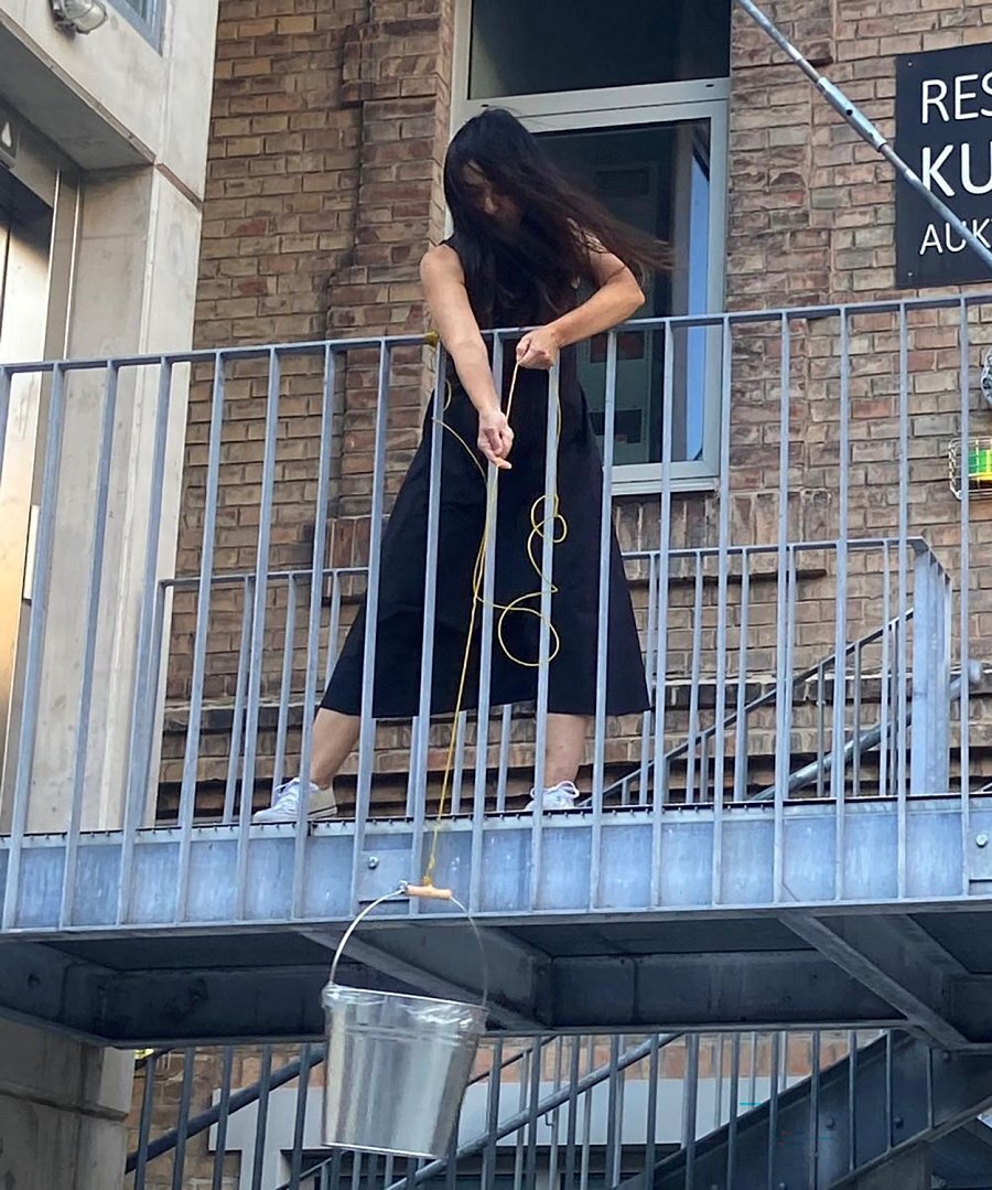 Eine Frau lässt einen Kübel an einem Seil ein Stiegengeländer hinab