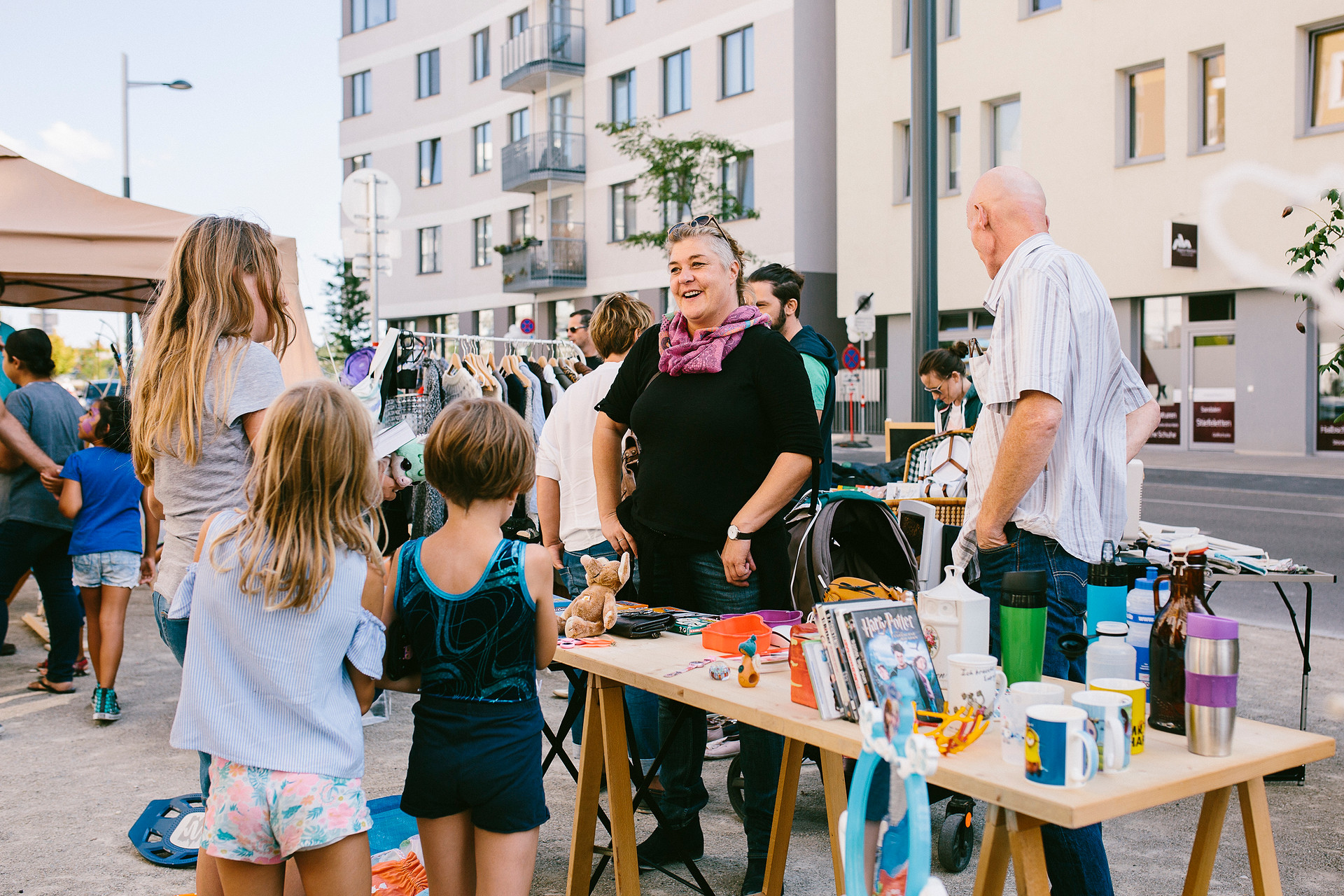 Frau steht vor einem Flohmarktstand und unterhält sich mit Kindern