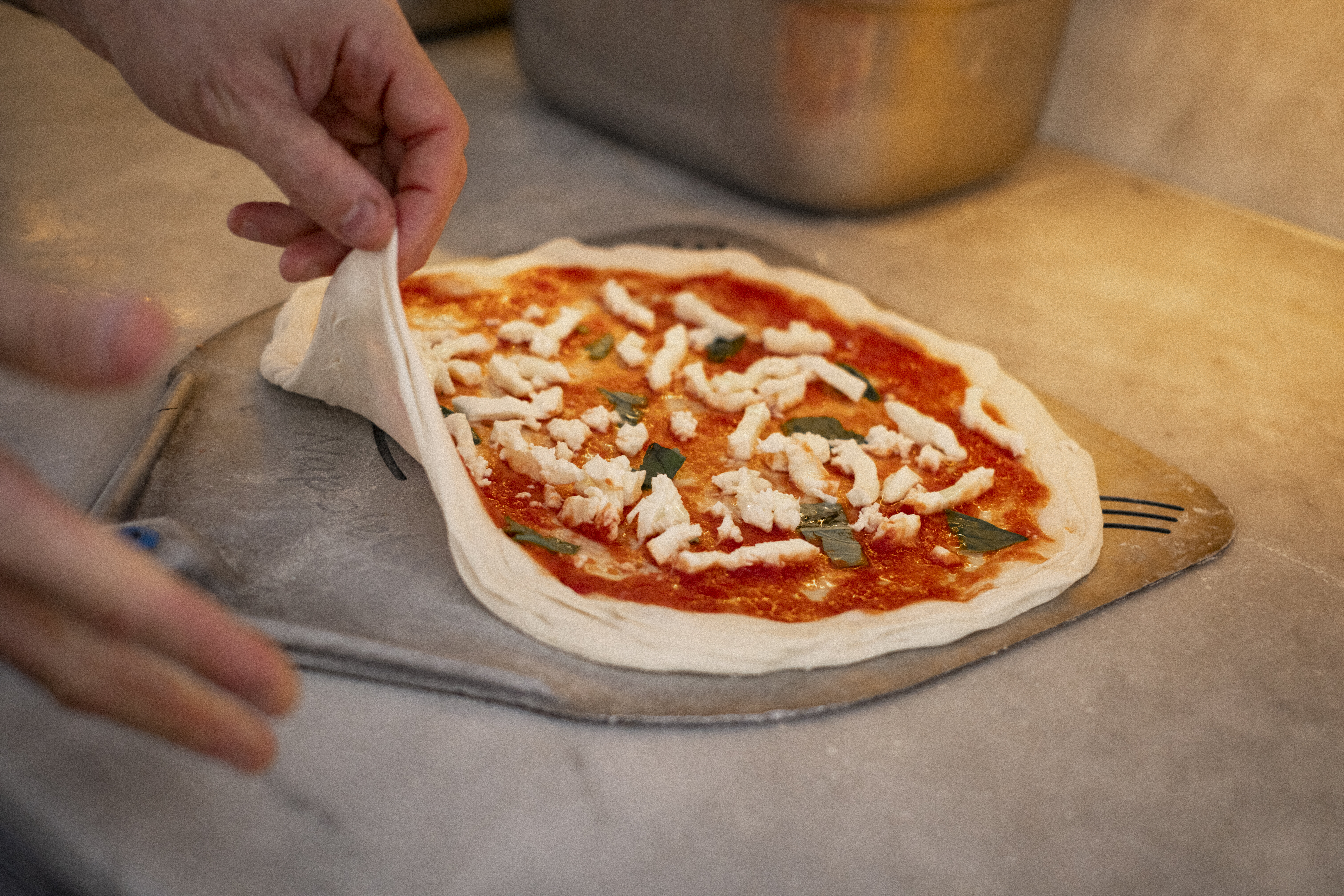 Man sieht Hände, die eine Pizza mit Sauce bestreichen