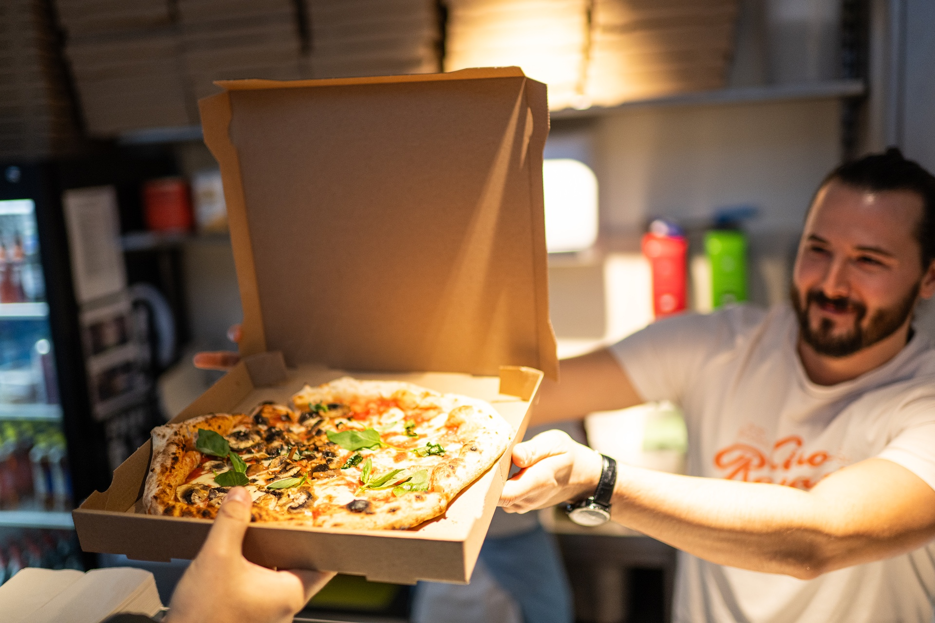 Pizzakarton wird von einem Pizzaverkäufer über die Theke zum Gast gereicht