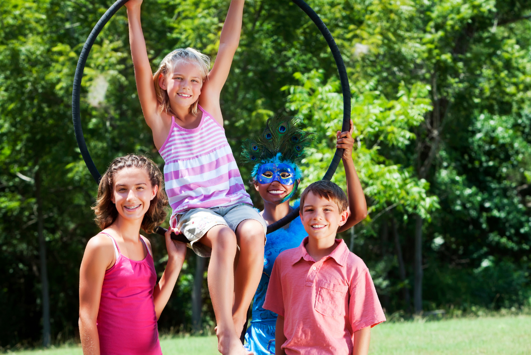 Vier Kinder lachen in die Kamera, eines sitzt in einem Hula-Reifen, der von den anderen Kinder gehalten wird