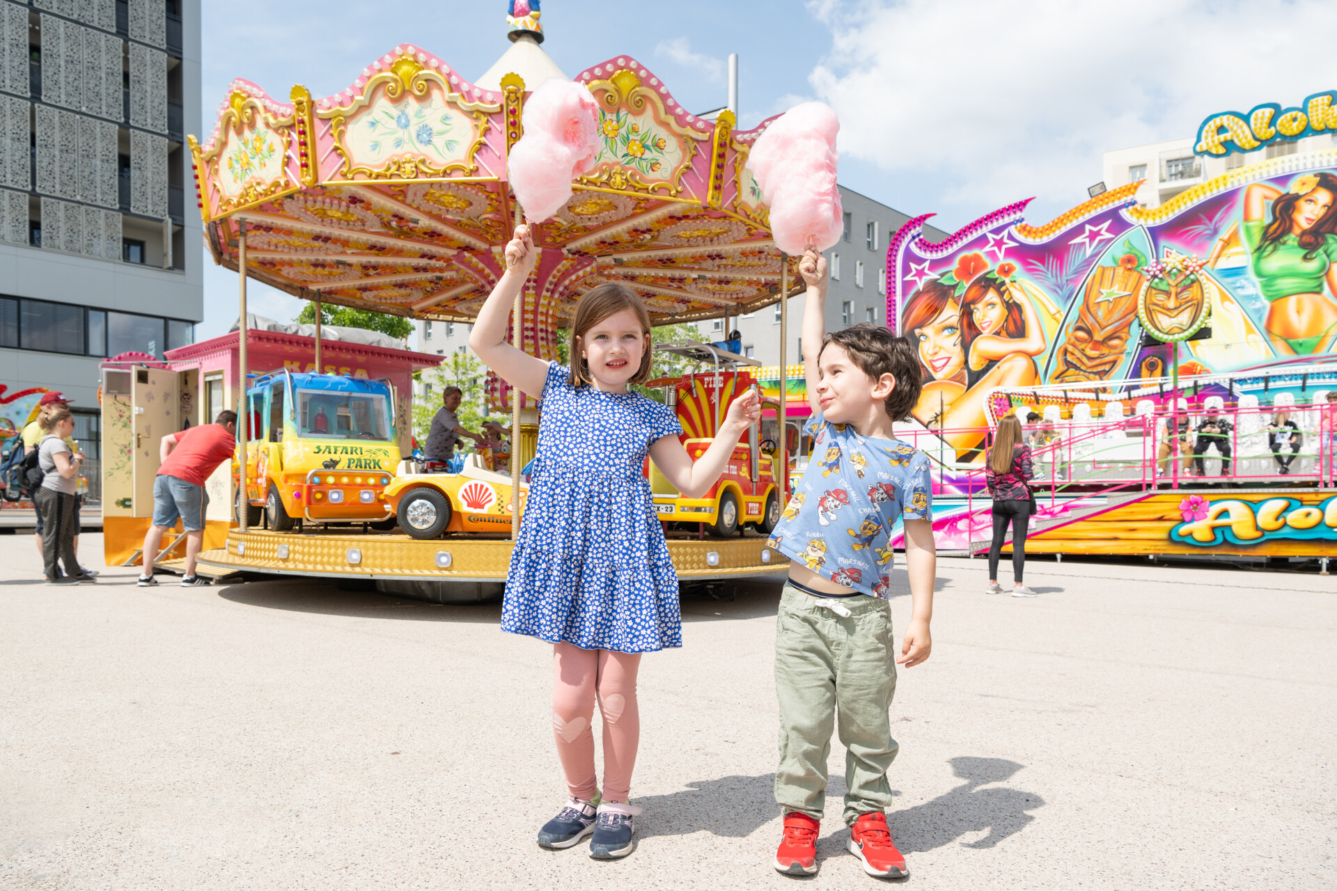 zwei Kinder halten eine Zuckerwatte in die Höhe und stehen vor Jahrmarkt-Fahrgeschäften beim Seestädter Kirtag