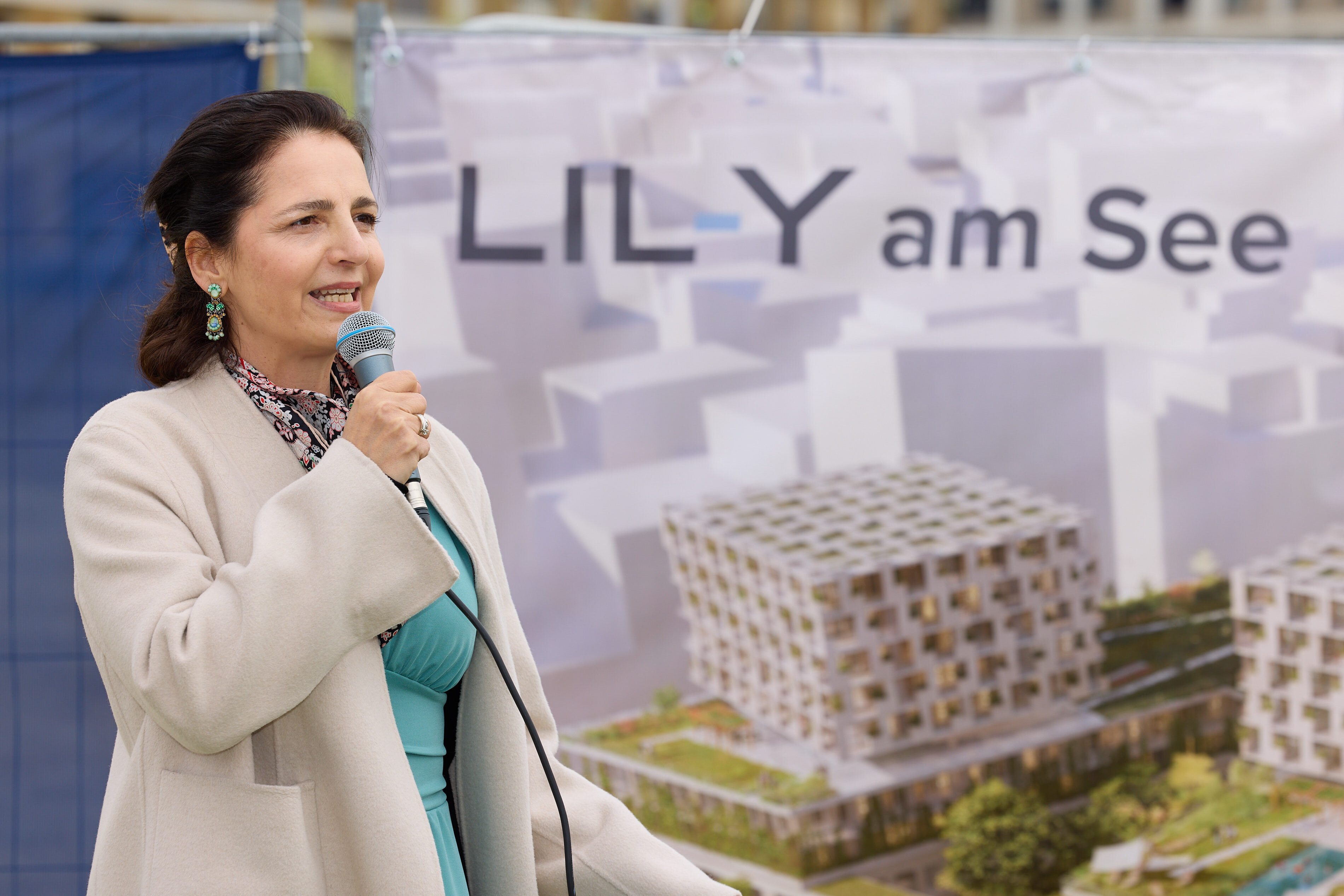 Frau spricht bei Projektvorstellung LILY am See vor Banner mit Visualisierung moderner Wohnanlage.