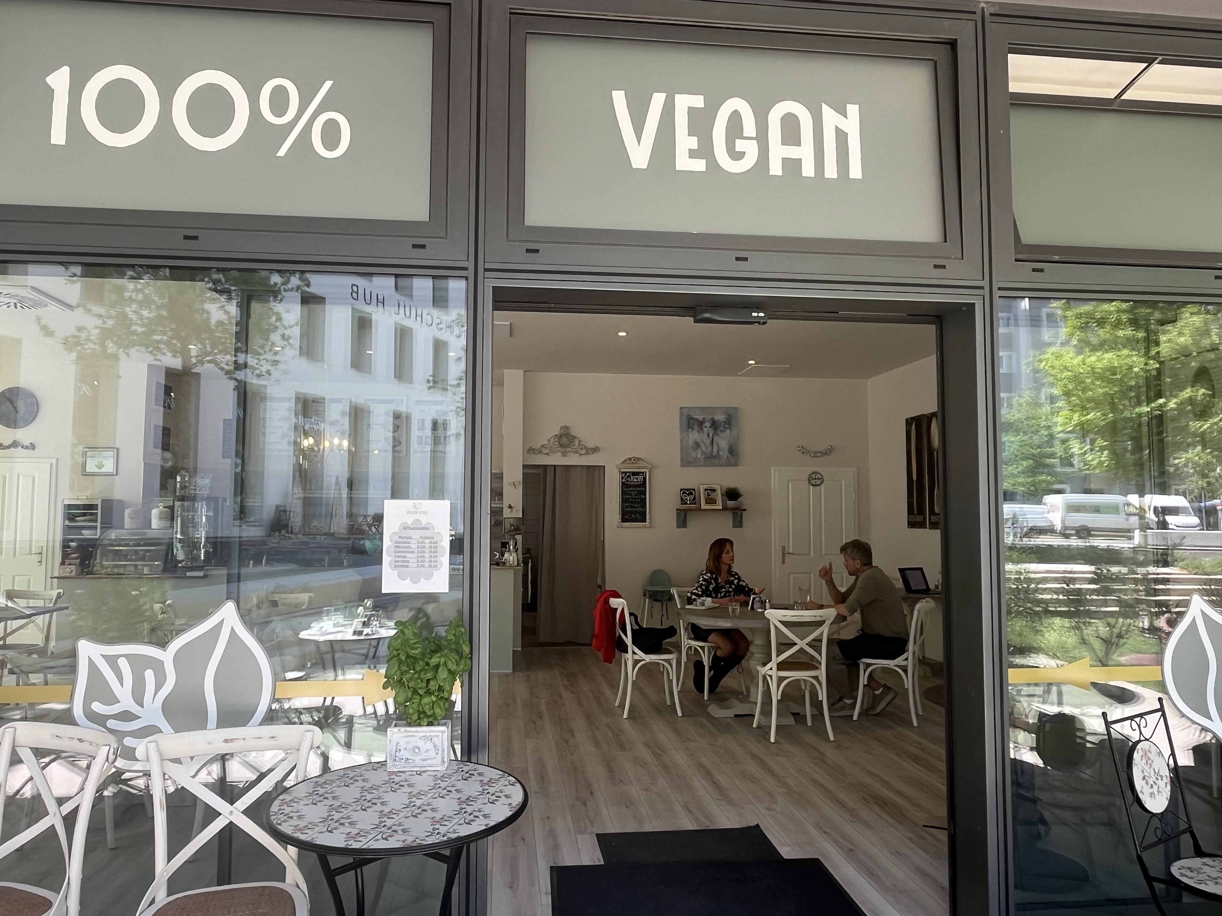Außenaufnahme des Cafés Vegan Kiss durch die Eingangstüre, es sind im Hintergrund zwei Personen an einem Tisch zu sehen, die sich unterhalten