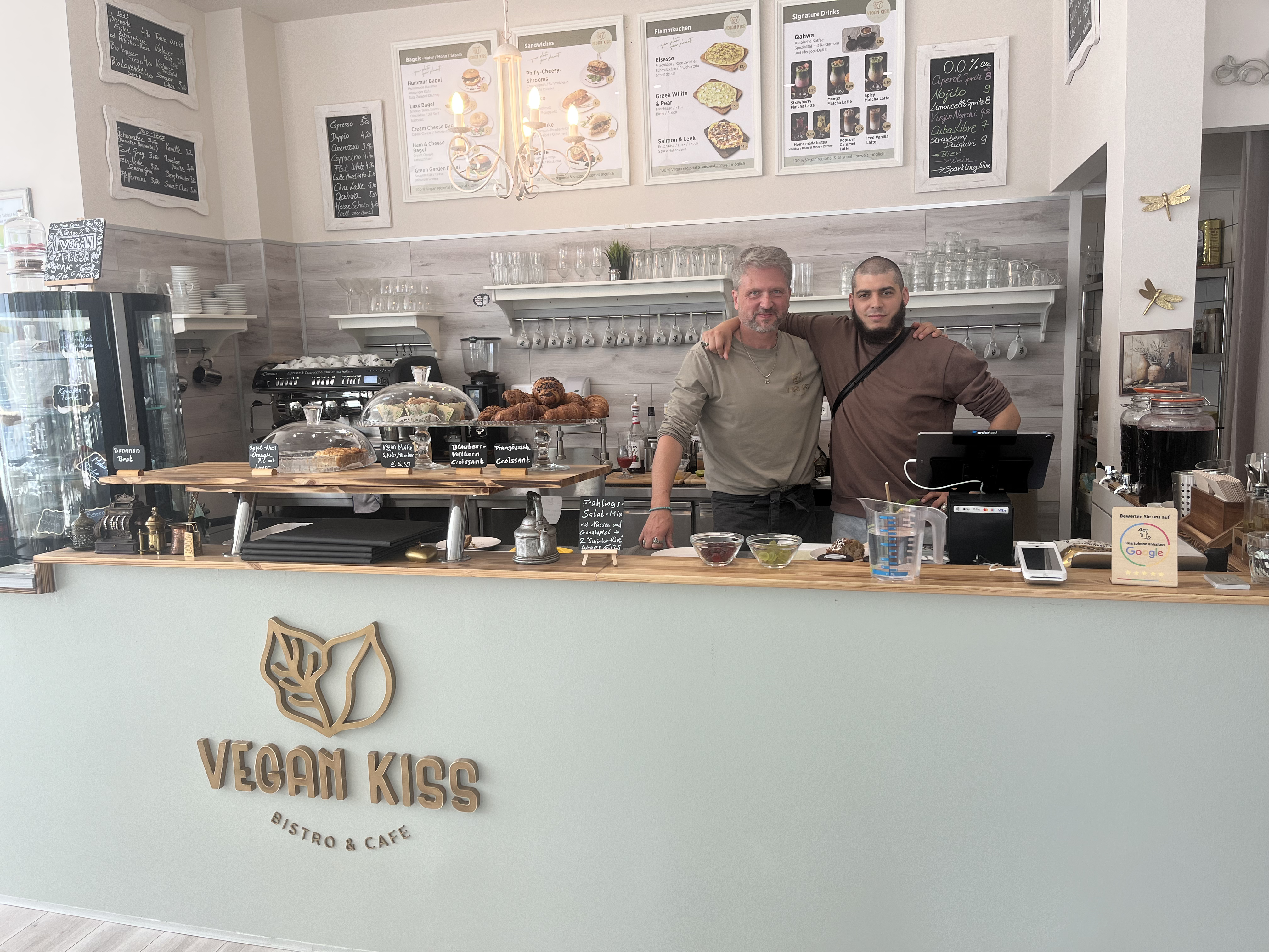 Besitzer des Cafés Vegan Kiss stehen hinter der Bar und umarmen sich 