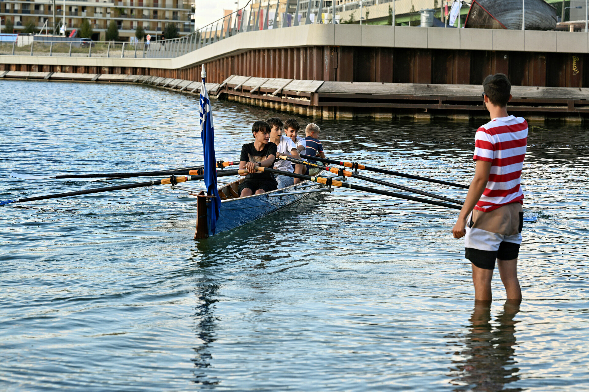 Mehrere Personen in einem Ruderboot, eine Person steht daneben im Wasser. 