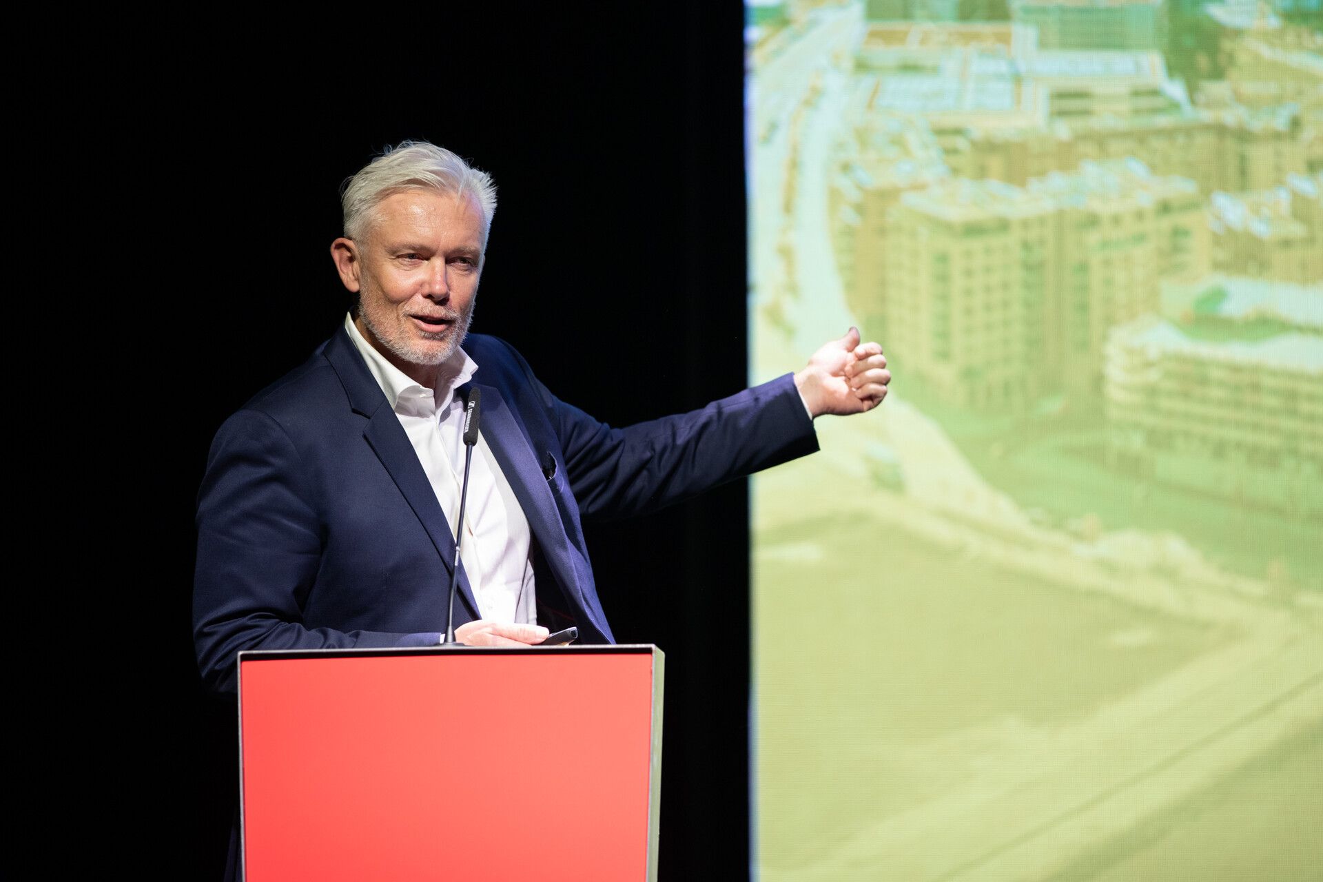 Robert Grüneis präsentiert ein Bauprojekt während einer Veranstaltung auf der Bühne.