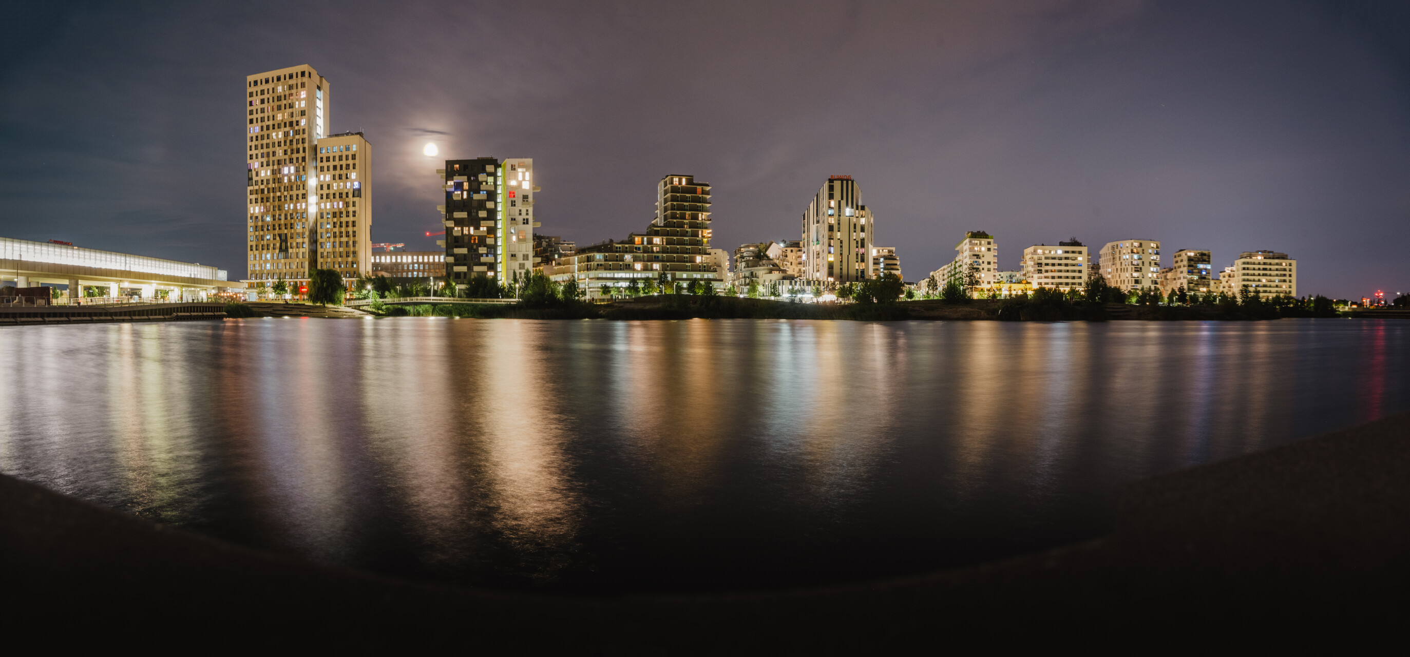 Skyline der Seestadt Aspern in Wien bei Nacht mit beleuchteten Wohngebäuden und Spiegelung im Wasser.