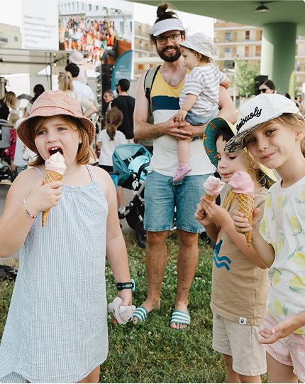 Kinder essen Eis. Ein junger Mann mit Kleinkind schaut in die Kamera und im Hintergrund sind viele Menschen auf einer Wise in der Stadt