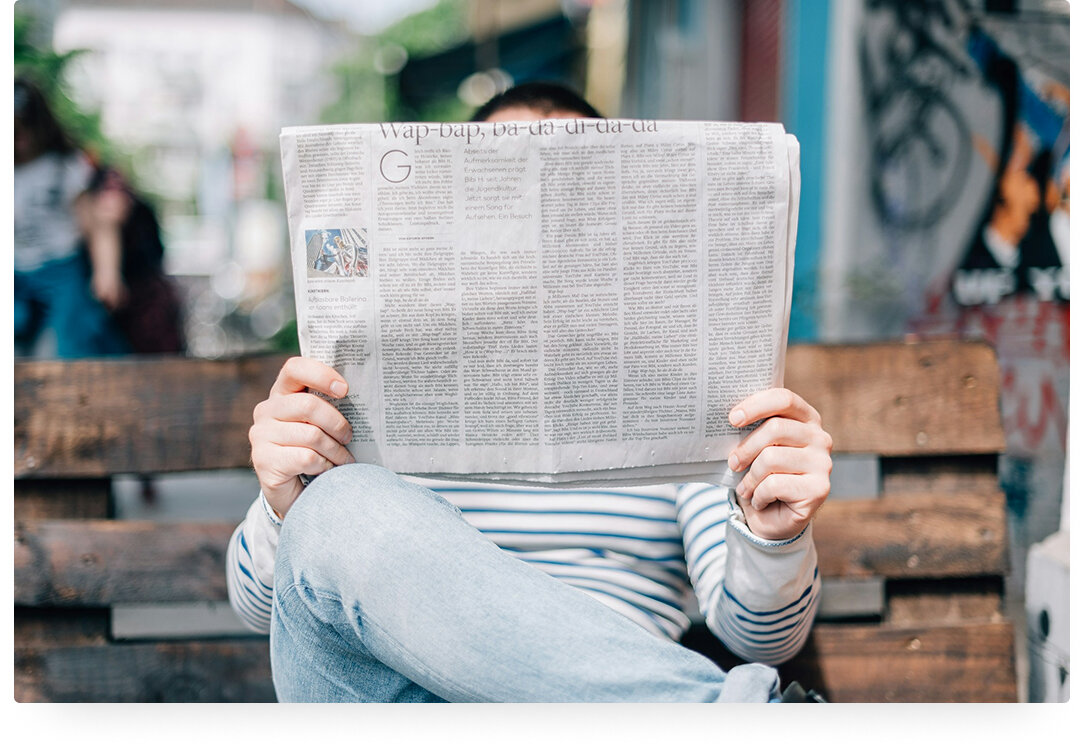 ein Mann sitzt auf einer Bank vor einer bunten Wand und liest eine Zeitung