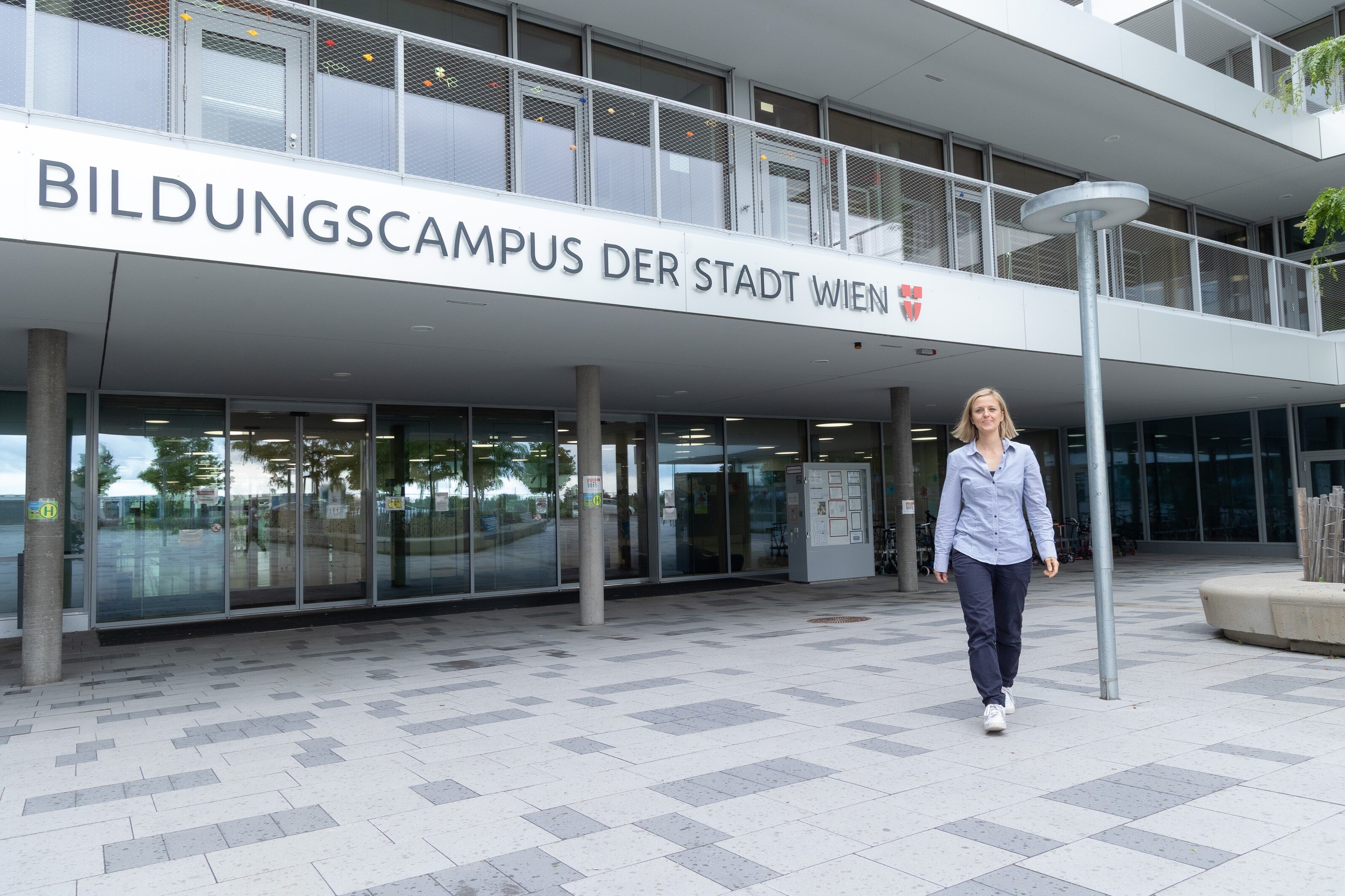 Blonde Frau geht vor dem Bildungscampus der Stadt Wien.