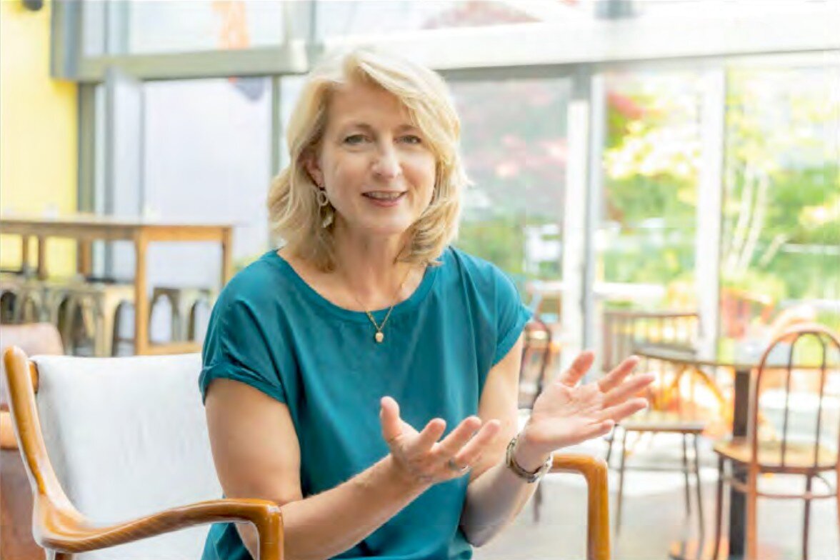 Frau mit blonden Haaren und blauem T-Shirt sitzt auf einem Stuhl.
