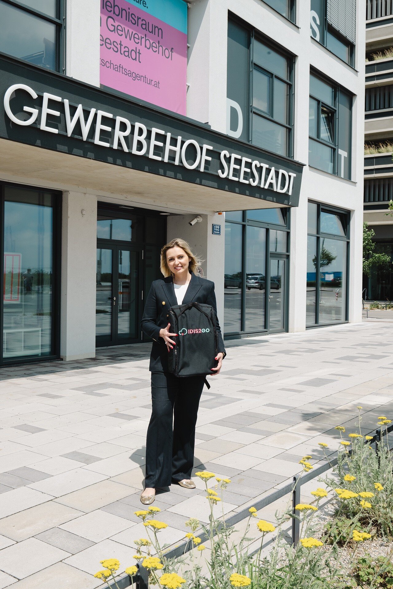Eine junge blonde Frau steht vor dem Gewerbehof Seestadt. 
