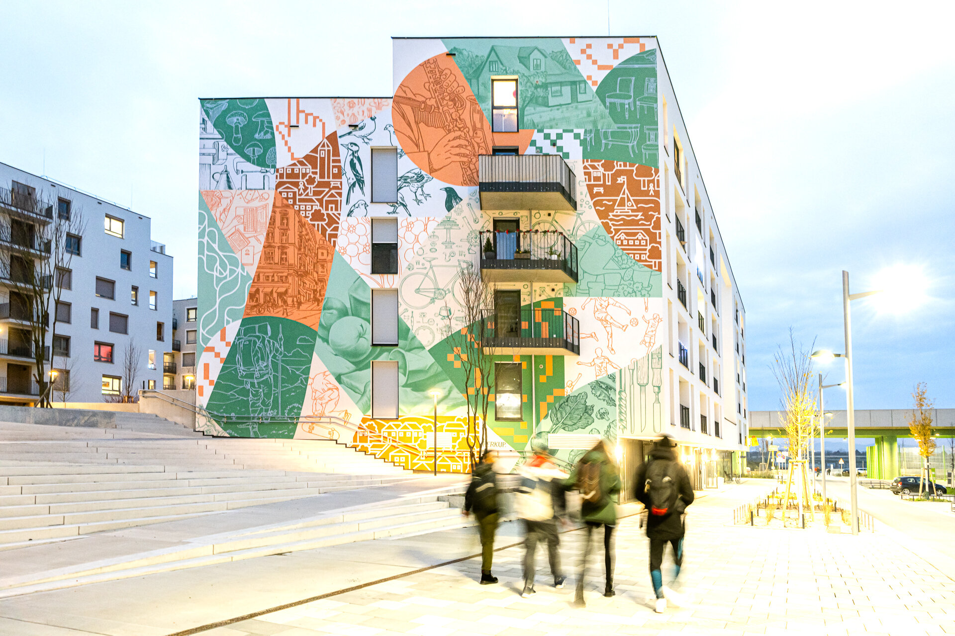 Eine Gruppe Menschen gehen an einem Wohnkomplex mit breiten Stufen, künstlerisch gestalteter Wand und vielen Balkonen Richtung U-Bahn