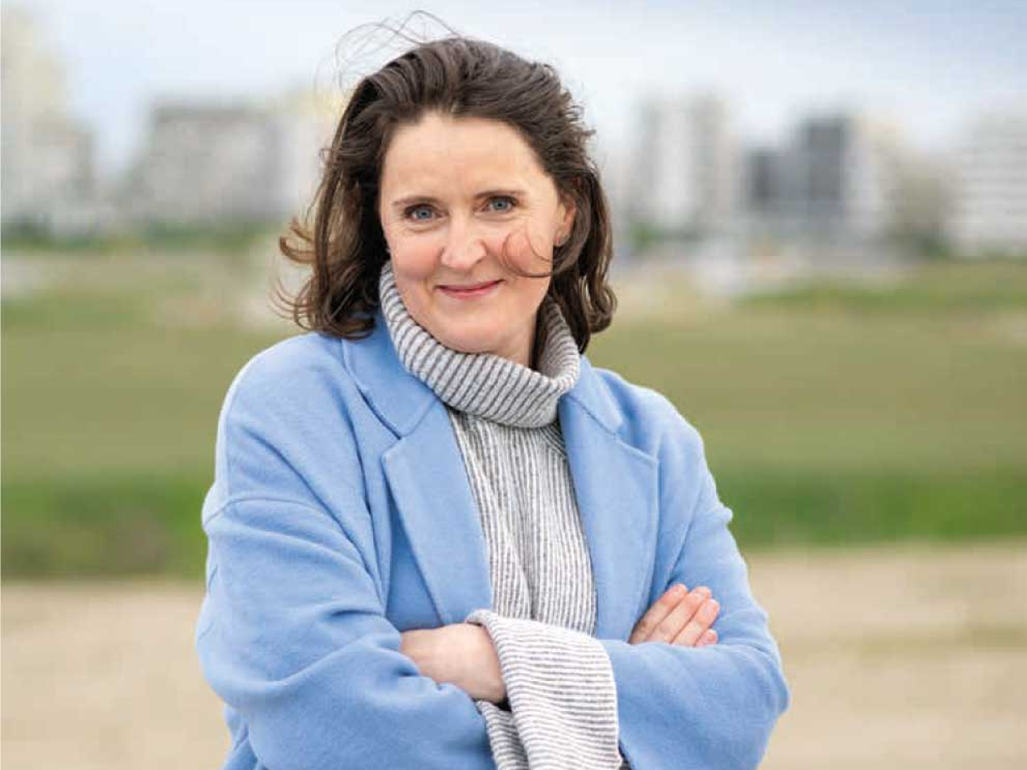Frau mit dunklen schulterlangen Haaren und hellblauem Mantel.