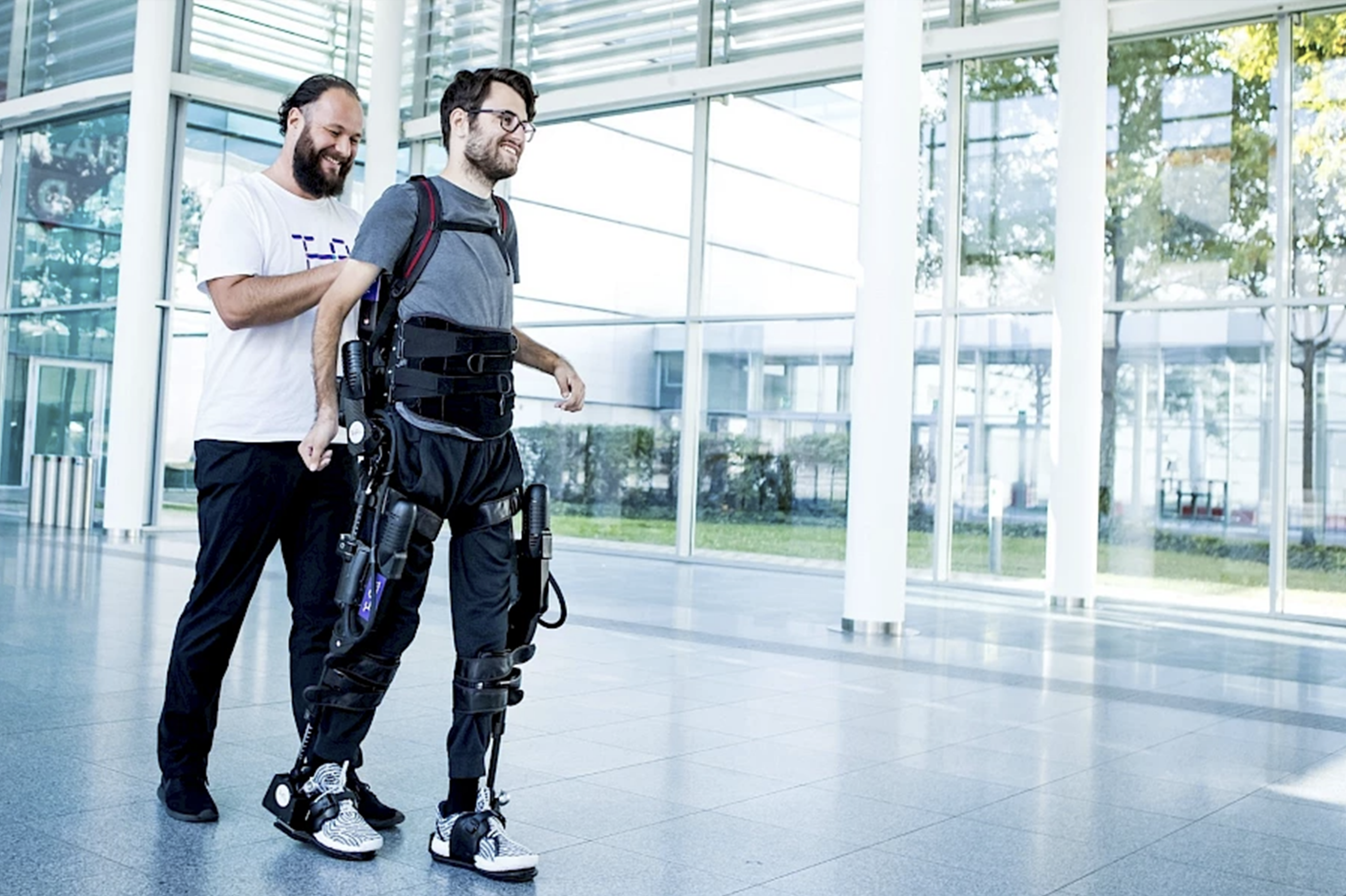 Ein Mann mit einem Exoskelett, dahiner ein anderer Mann. 