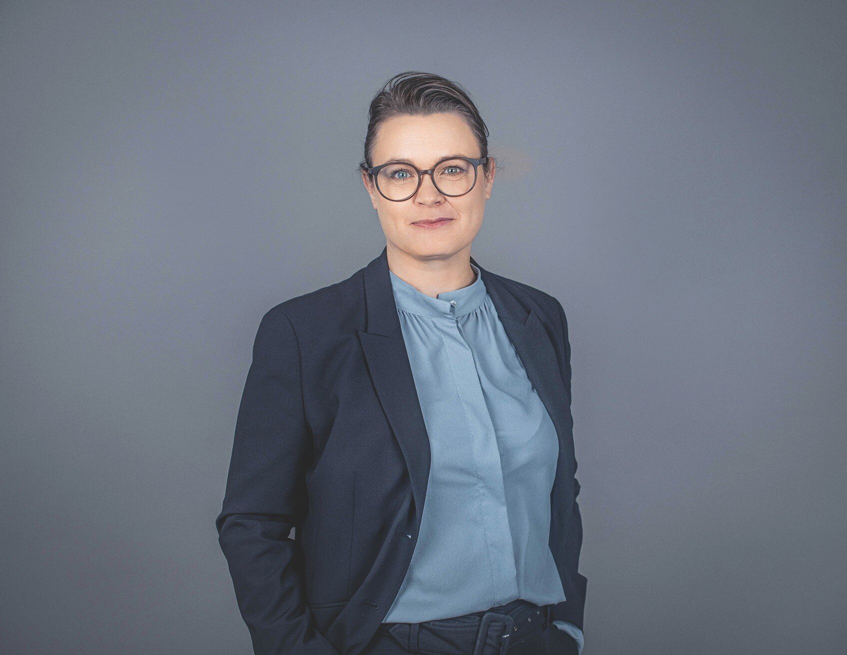 Frau mit Brille, dunkelblauem Blazer und einer hellblauen Bluse.
