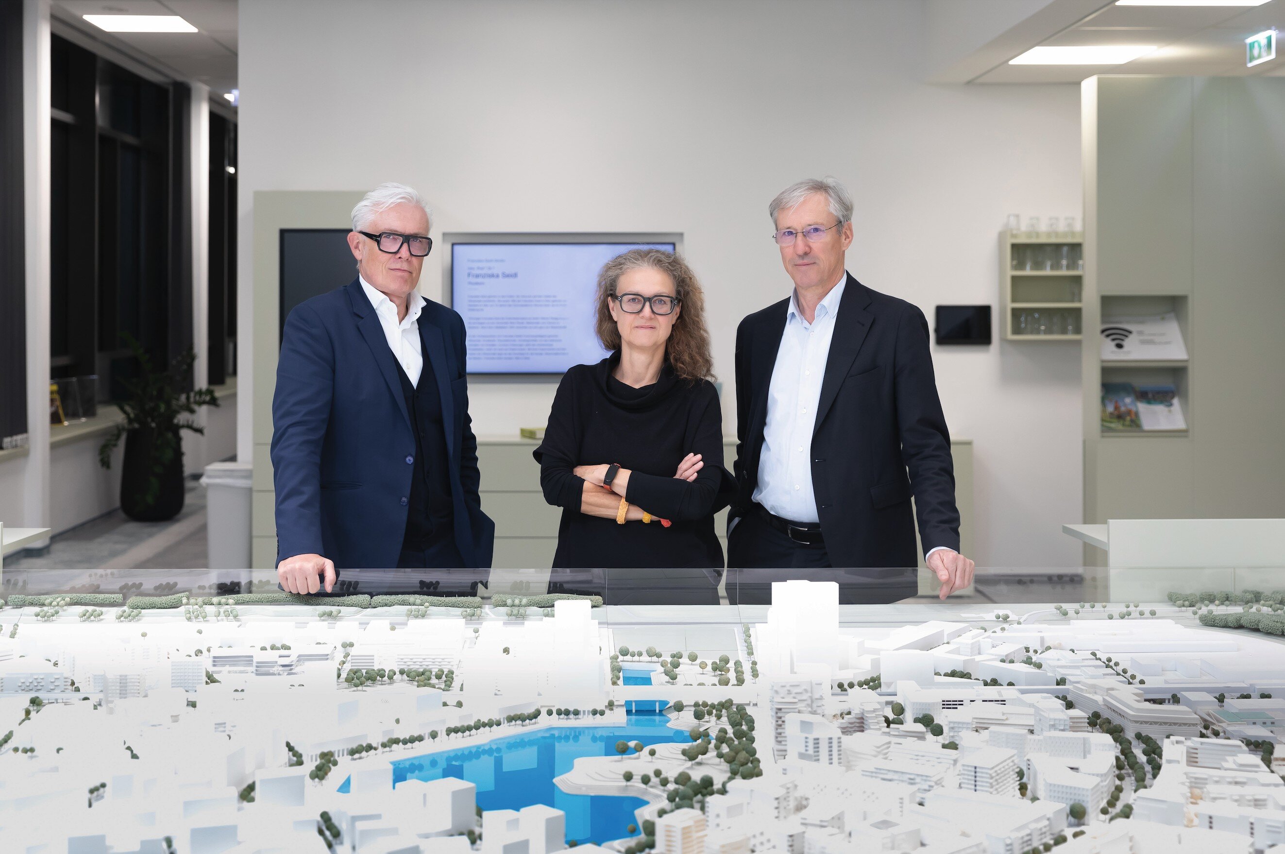 Zwei Männer und eine Frau stehen vor einem Architekturmodell. 