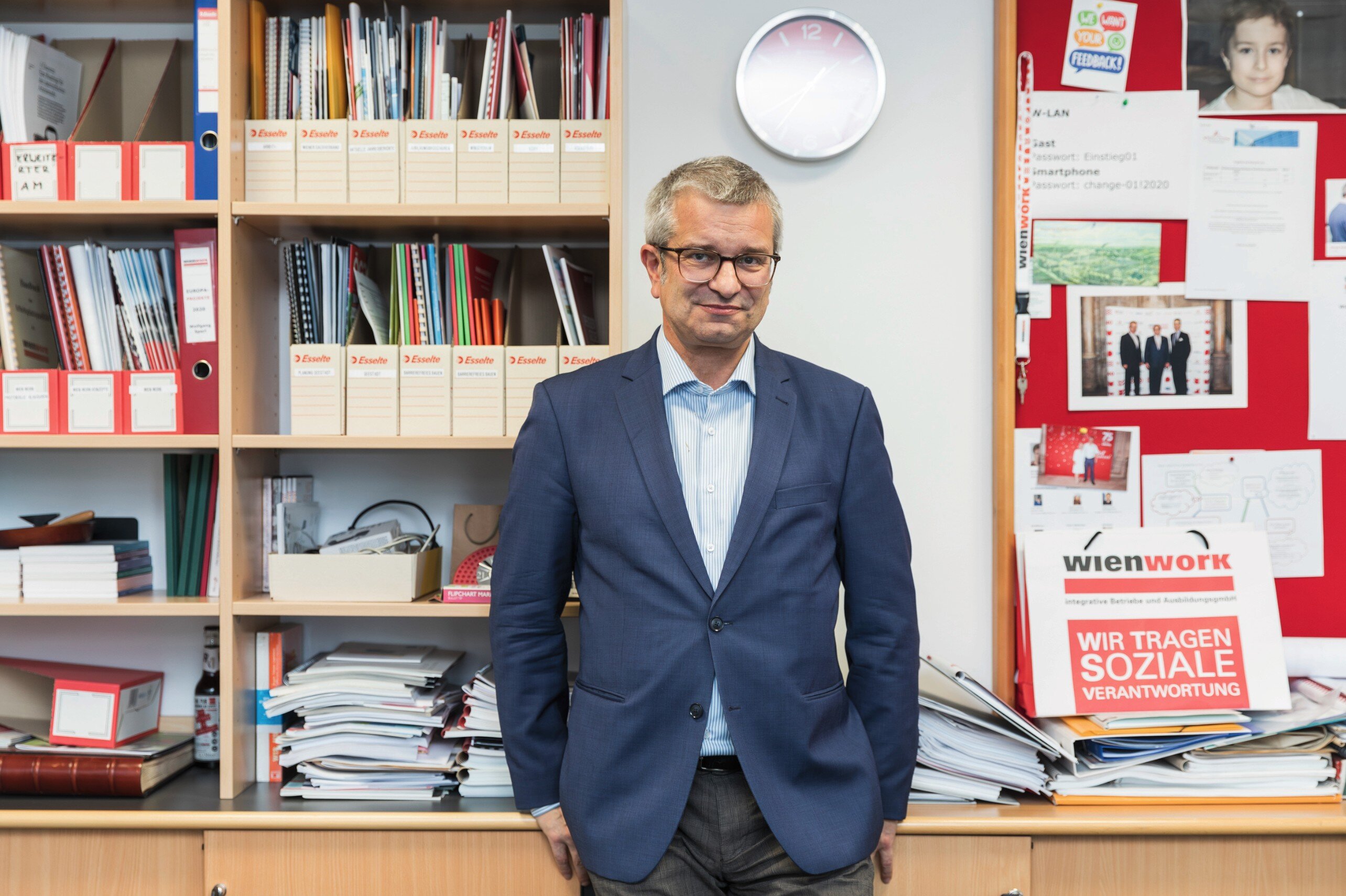 Mann in Anzug steht vor Büroregalen. 