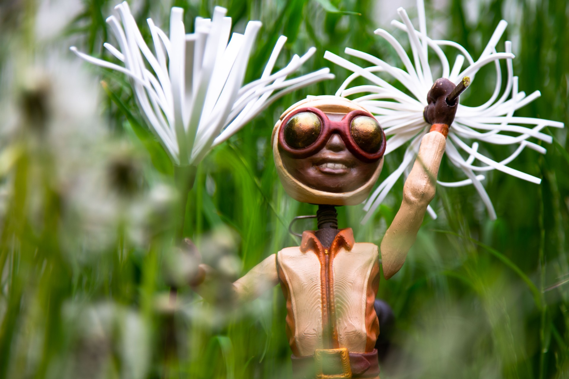 Eine Riesenameise im Anzug und mit Brille steht im Gras und hält einen weißen Löwenzahnsamen in der Hand