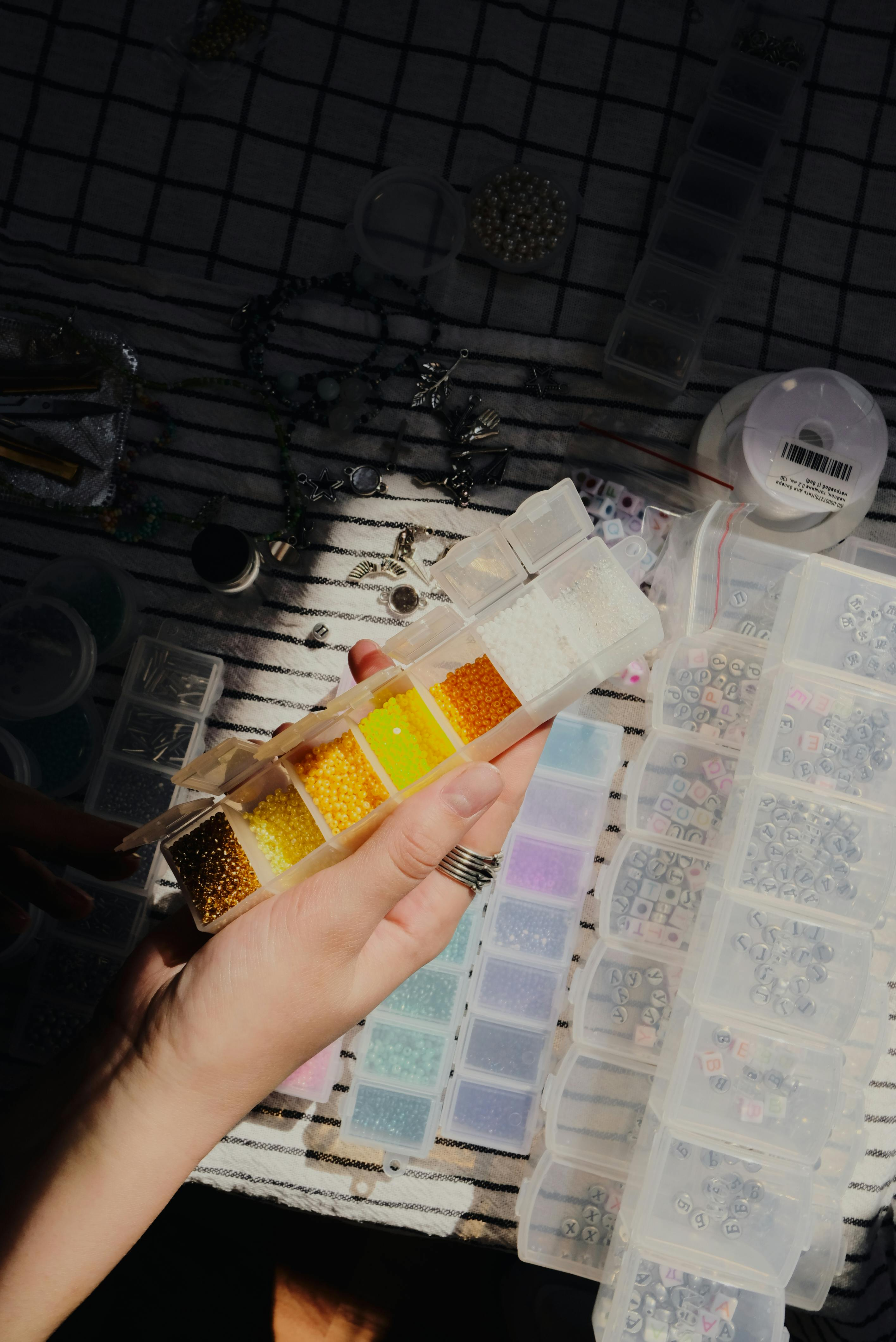 Eine Hand hälte eine offene Box mit mehreren Unterteilungen, in denen sich gelb- und orangefarbene Bastelperlen befinden