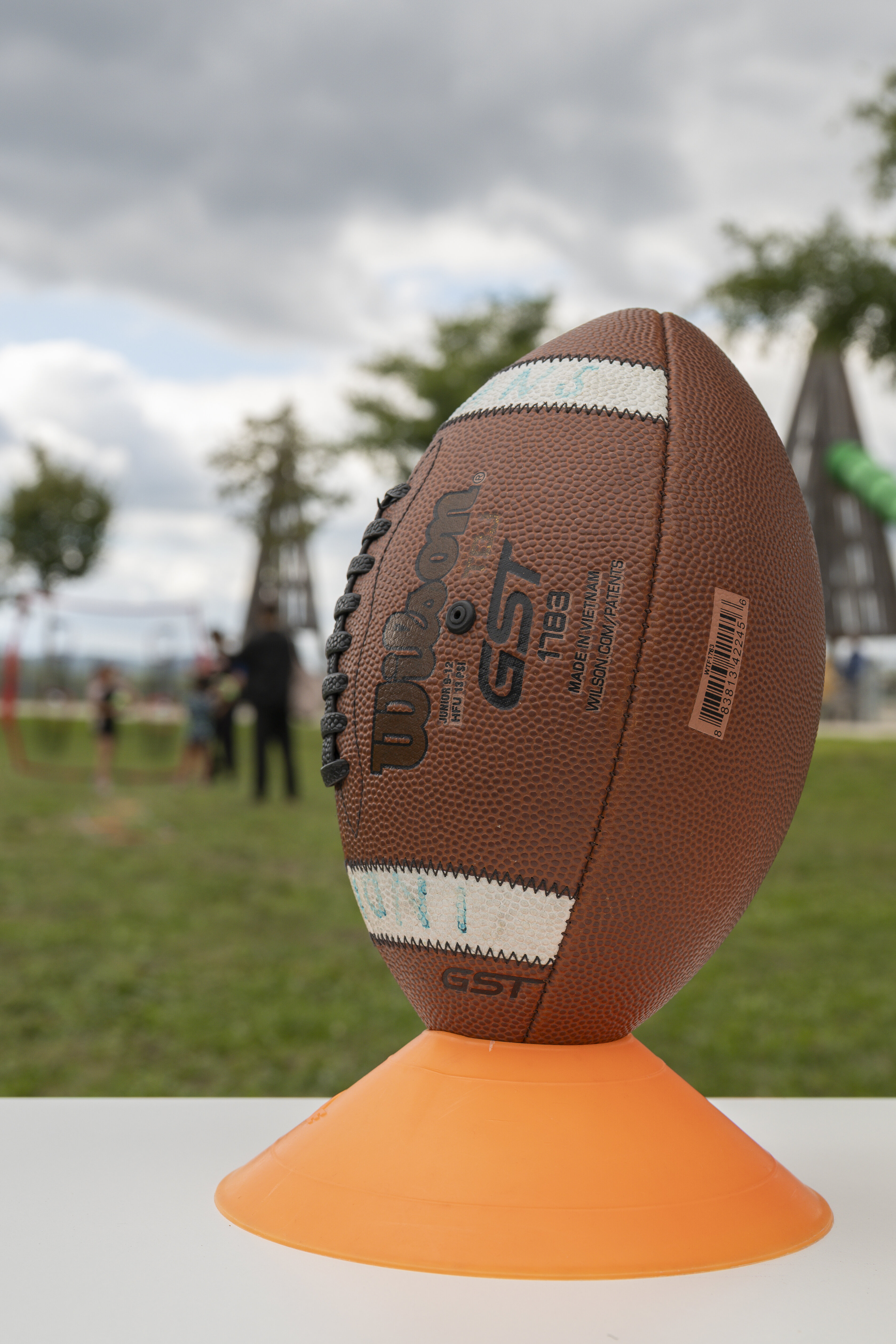 Ein Football steht auf einem Hütchen, im Hintergrund ist ein Park zu sehen. 