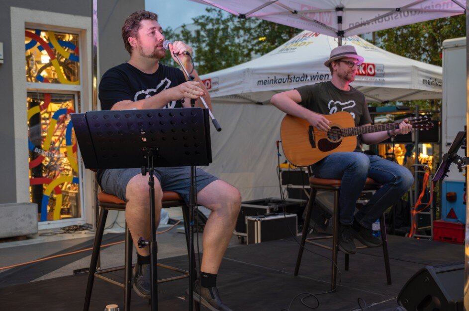 Zwei Musiker mit Gitarre und Hut sitzen in einem Zelt 