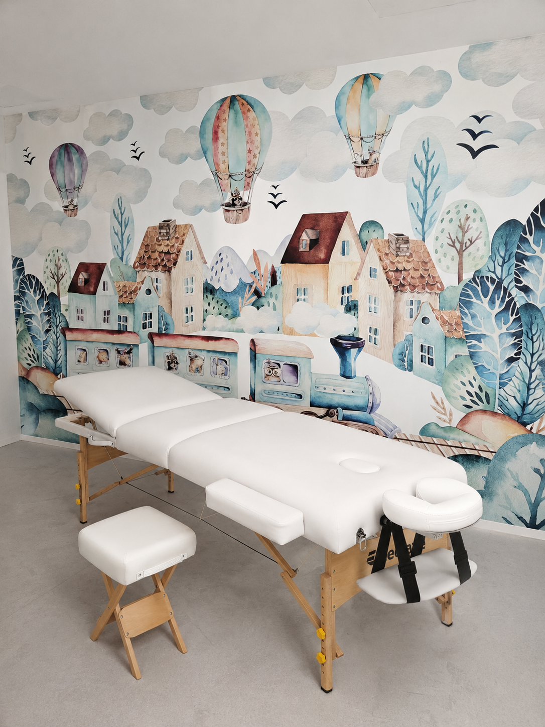 Massagetisch vor einer bunt tapezierten Wand mit Wolken- und Ballon-Muster