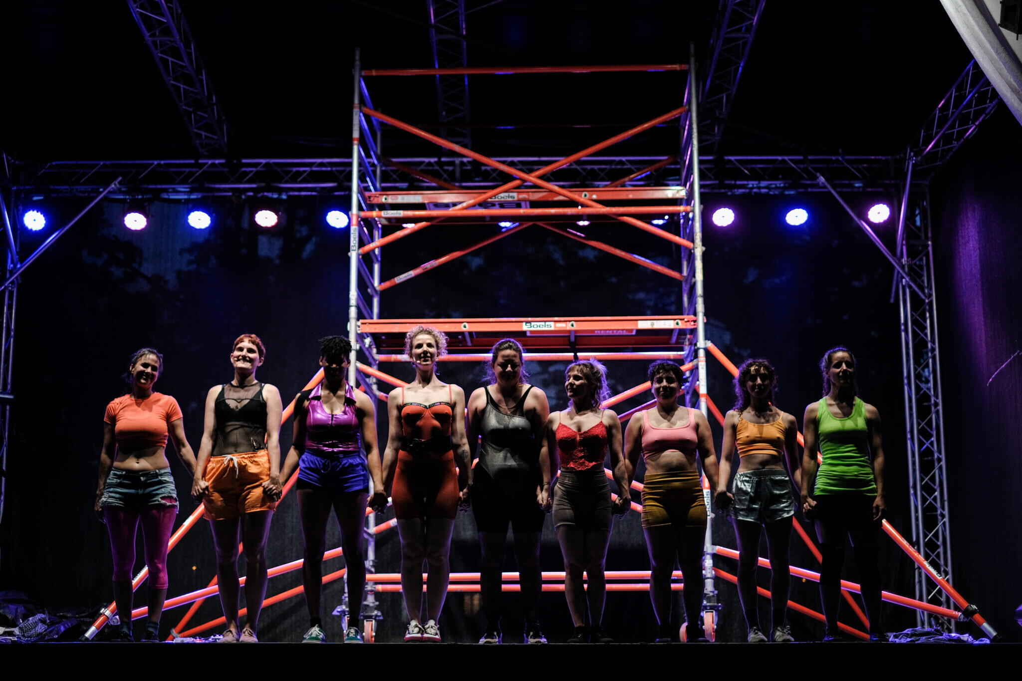 Gruppe von Frauen auf einer Bühne in sportlichen Outfits, die sich an den Händen halten