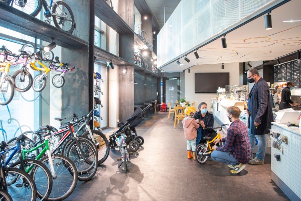 Personengruppe mit Kind
                                    in einem Fahrradgeschäft, Links Räder, rechts im Hintergrund Cafe-Bar. 