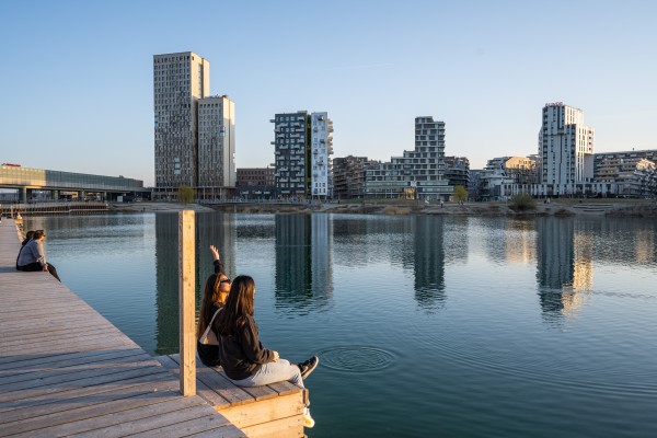 Menschen
                                    sitzen am See mit der Skyline von aspern Seestadt im Hintergrund