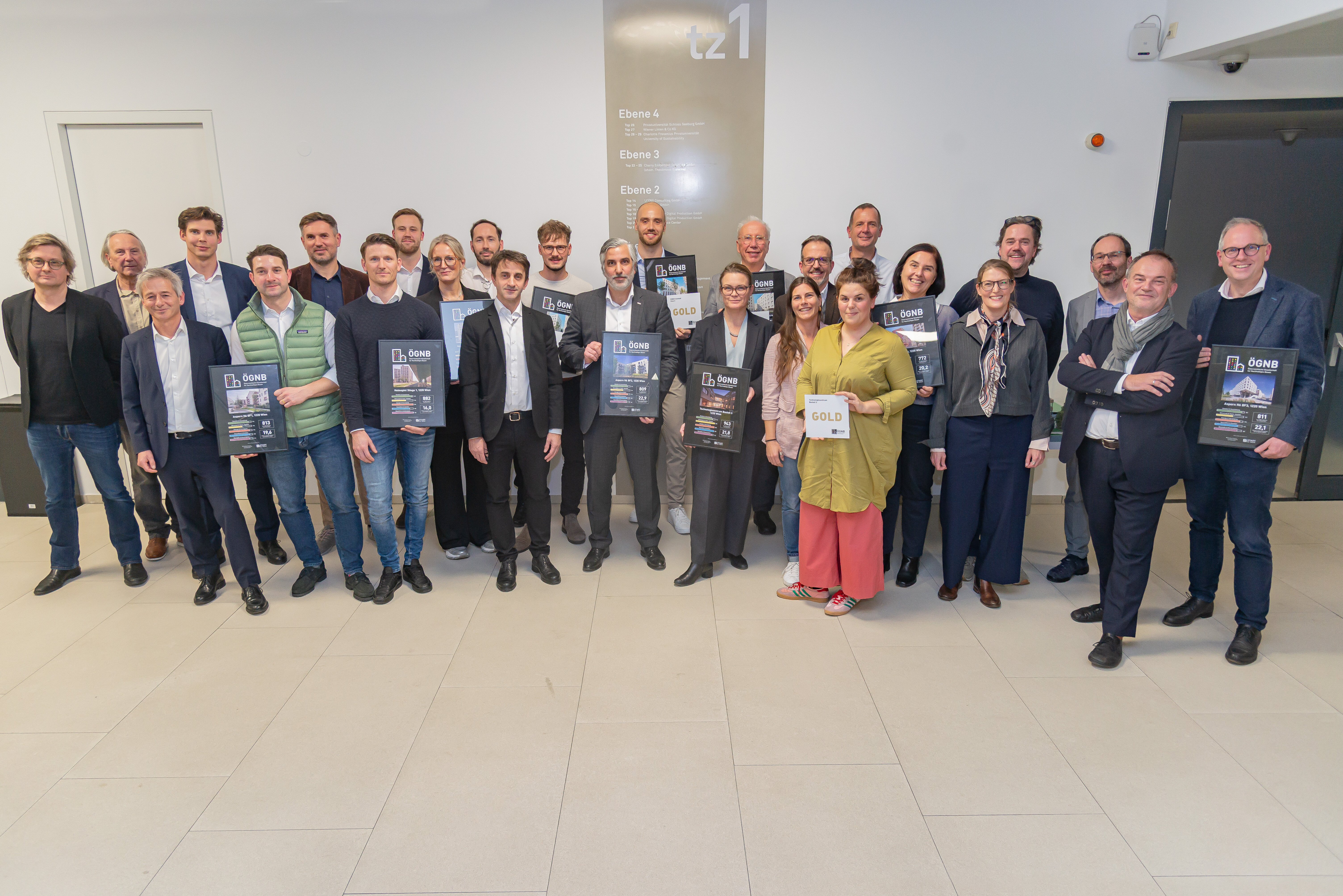 Gruppenfoto mit vielen Menschen, die in die Kamera Blicken und ein Zertifikat in der Hand halten