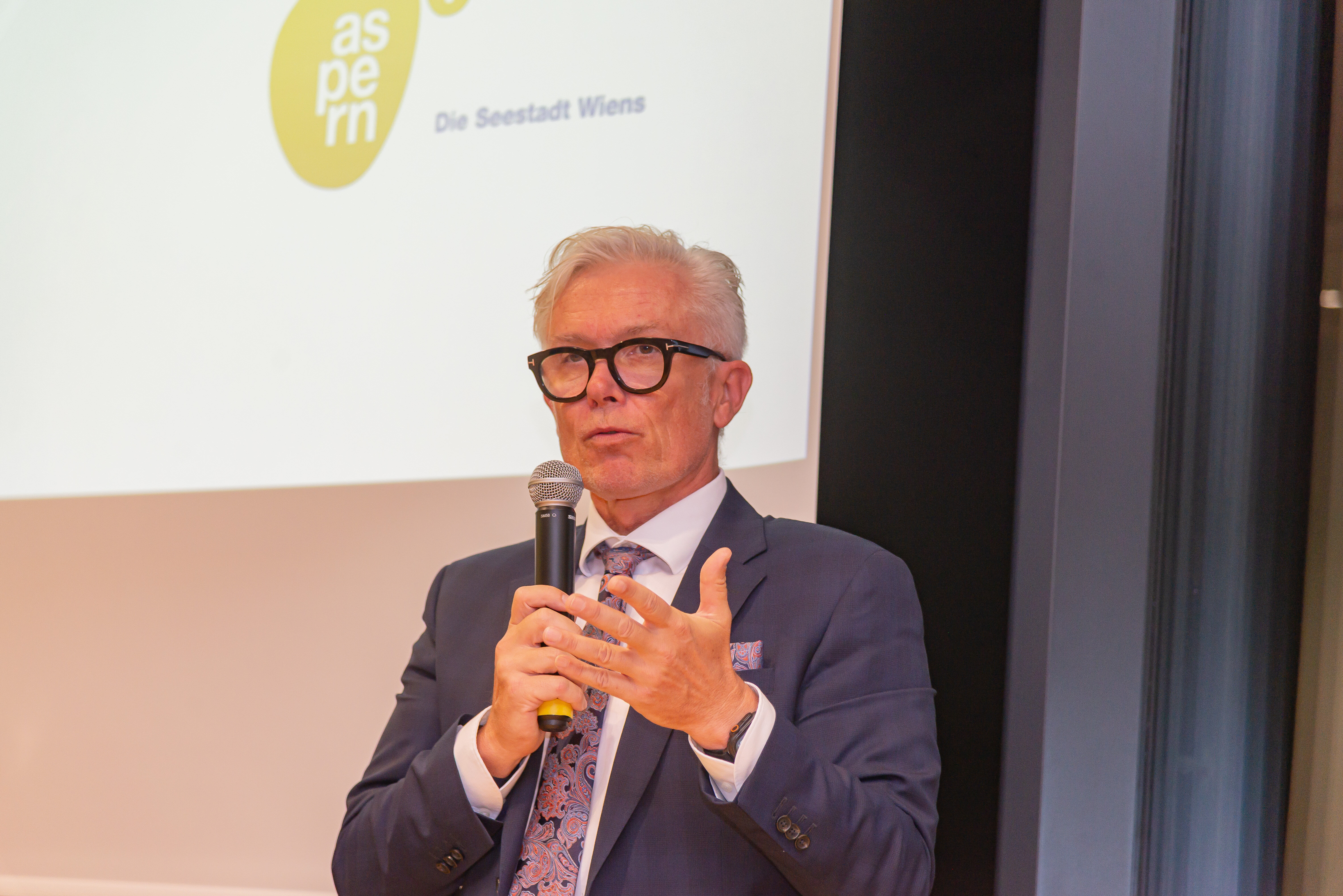 Mann spricht in ein Mikrofon, es ist nur der Oberkörper geschrieben.